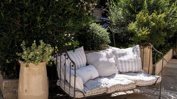 A wrought iron outdoor sofa with striped cushions, positioned next to a large planter with a small tree.