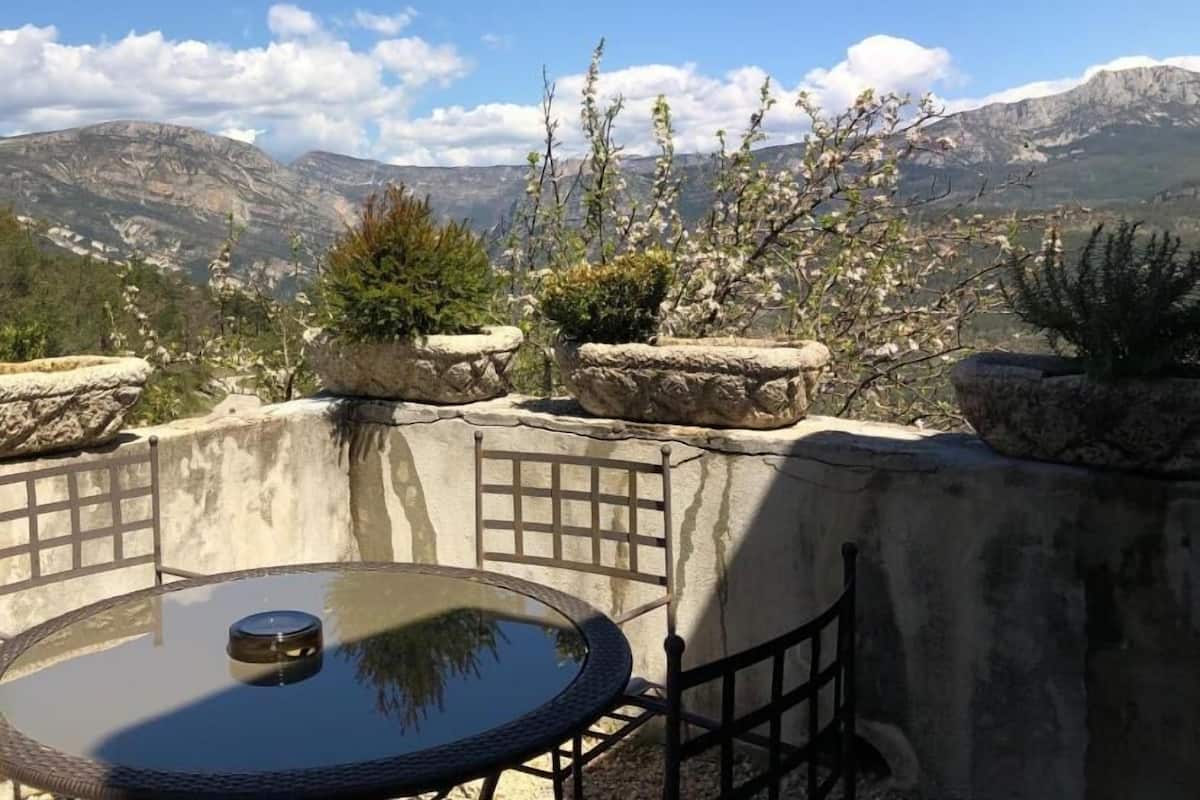 A terrace with a glass table and chairs, overlooking a mountainous landscape.