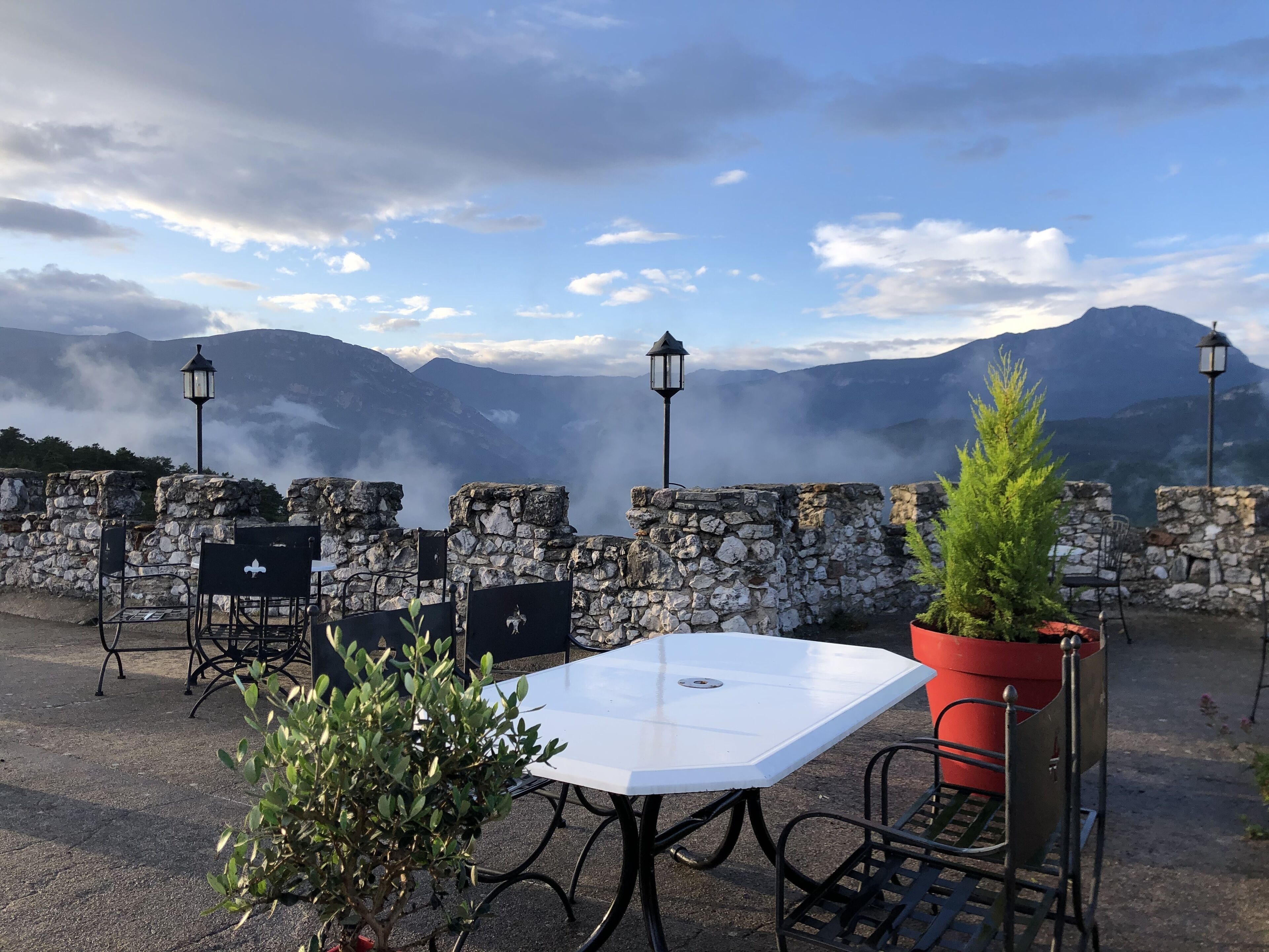 A stone wall with a table and chairs, a potted plant, and a view of mountains.