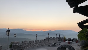 Un espacio al aire libre con paredes de piedra, mesas y sillas, faroles de piedra y vistas a montañas distantes.