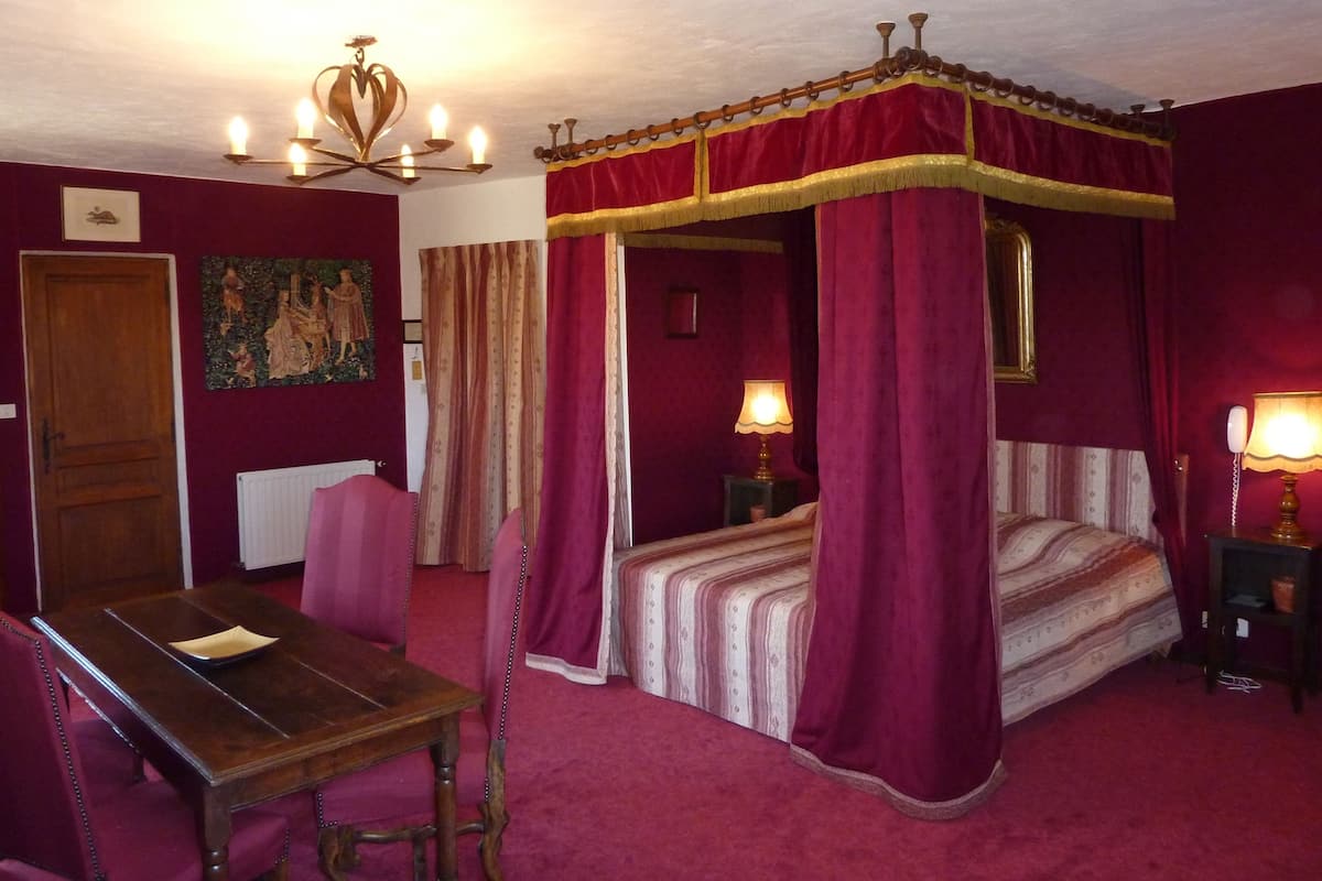 A bedroom with a four-poster bed, a wooden table, and two bedside lamps.