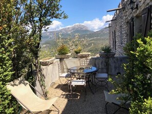 An outdoor patio with a table and chairs, surrounded by stone walls and potted plants, overlooking a mountainous landscape. - Château de Trigance (Trigance)