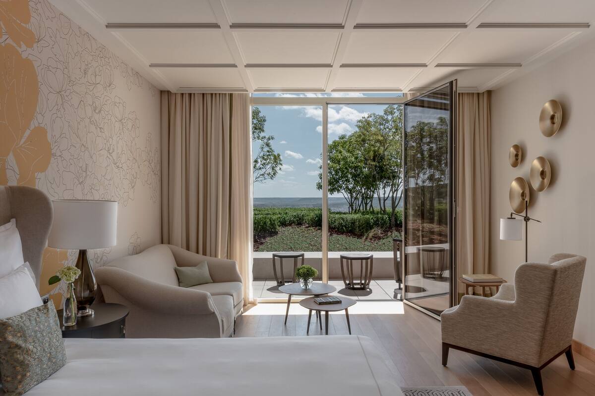 Une chambre d’hôtel moderne dotée d’un grand lit, d’un canapé, d’un fauteuil, d’une petite table et offrant une vue sur l’extérieur.