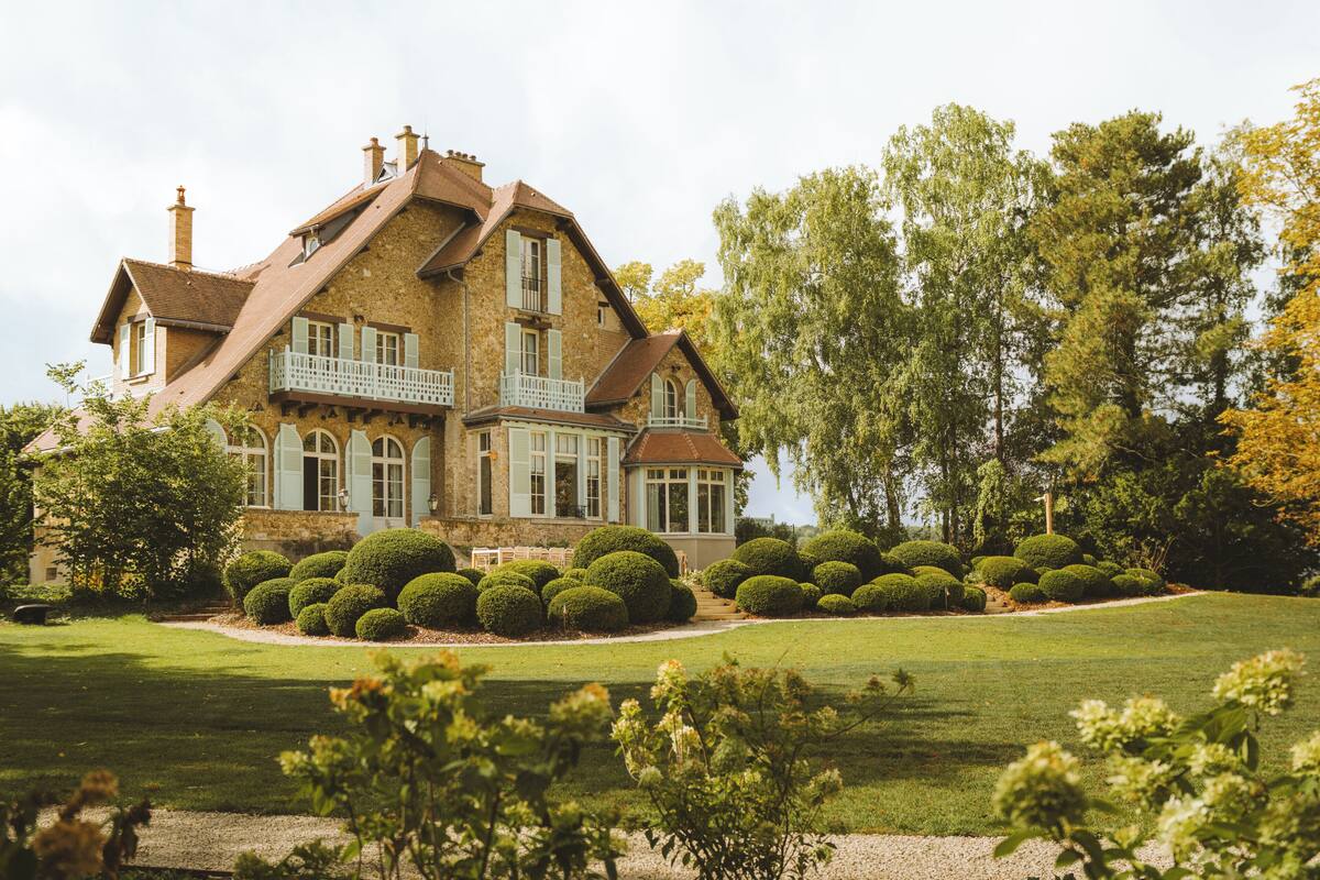 Une grande maison historique à la façade symétrique, dotée de nombreuses cheminées et d’un balcon.