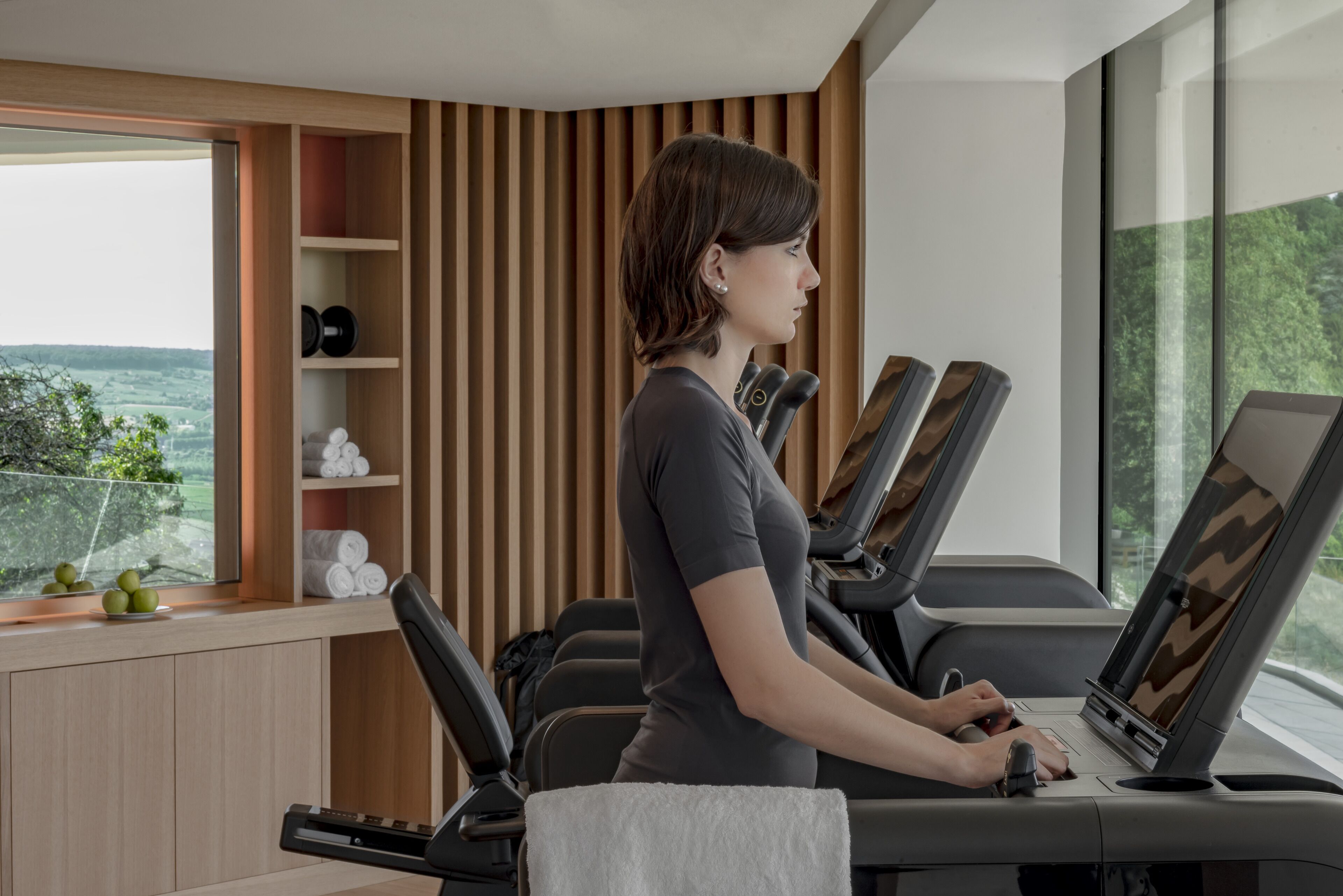 A modern gym with exercise equipment and a large window offering a view of greenery.