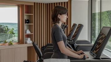 Un gimnasio moderno con equipamiento de ejercicio y un amplio ventanal con vistas a zonas verdes.