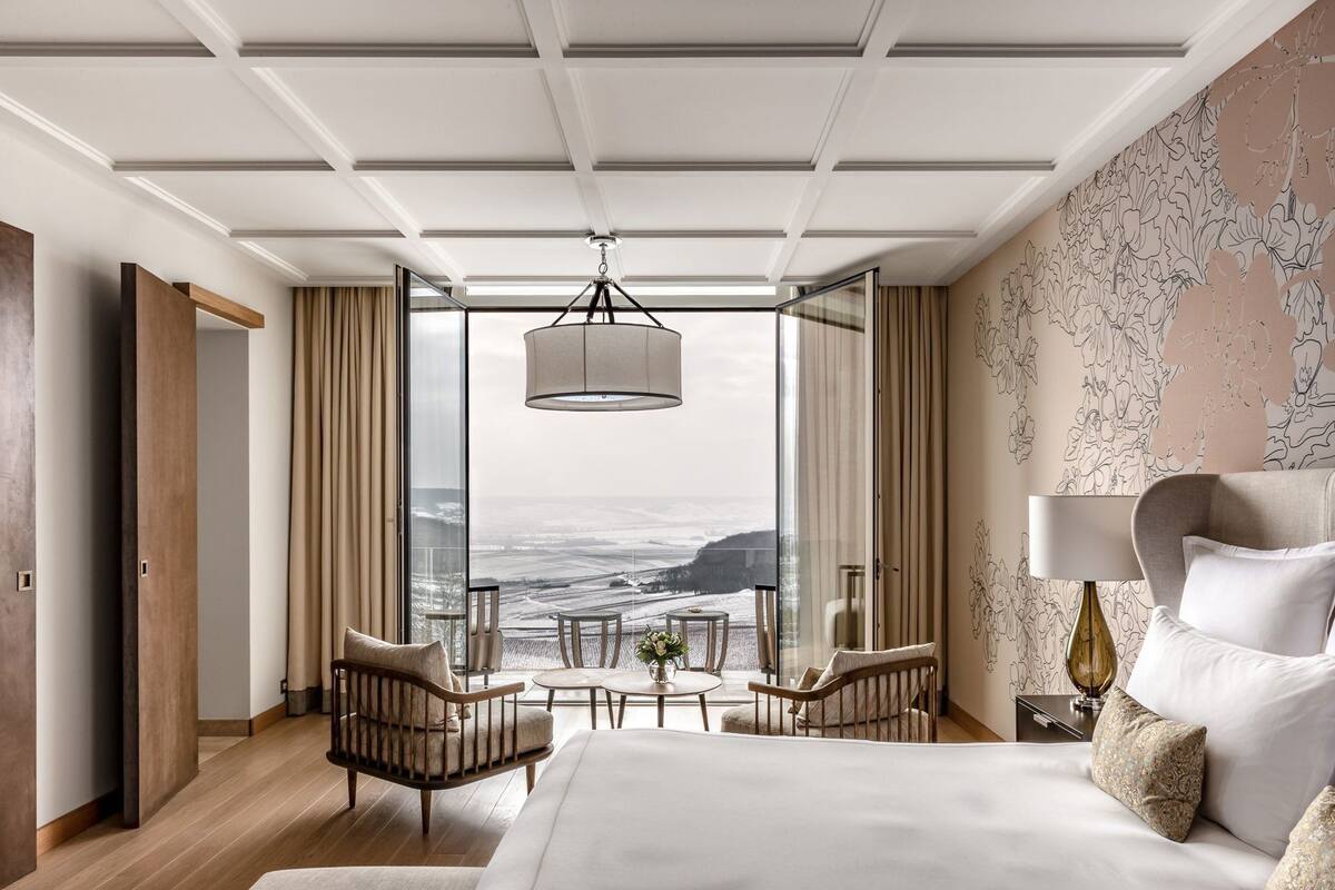 Une chambre d’hôtel moderne dotée d’un grand lit, d’un coin salon avec des fauteuils et une table, et offrant une vue sur l’océan.