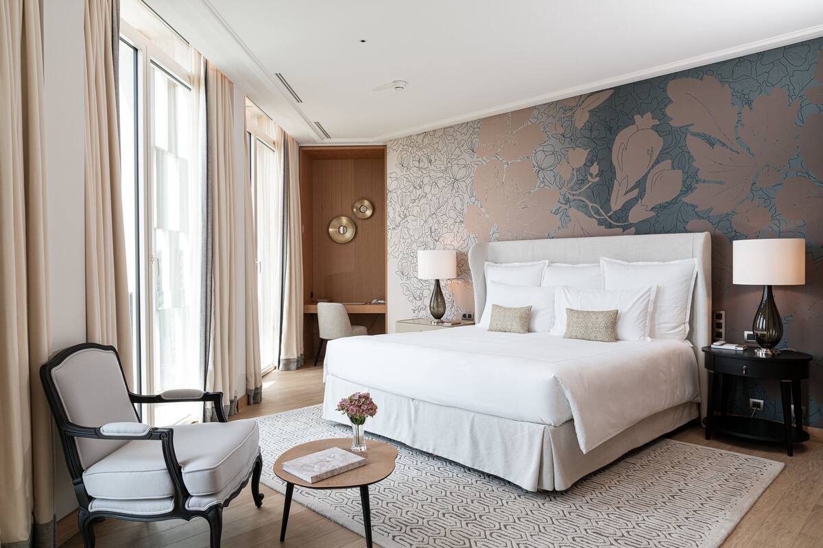 Une chambre d’hôtel avec un grand lit, un bureau, une chaise et une petite table sur laquelle est posé un vase de fleurs.