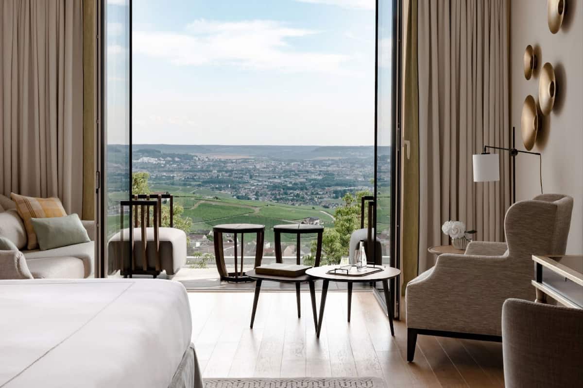 Une chambre d’hôtel moderne dotée d’une grande fenêtre, d’un lit, d’un canapé, d’une table à manger et d’une chaise.