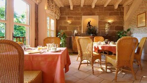 A dining area with wicker chairs and tables, stone walls, and a view of greenery outside. - Chateau de Castel Novel (Saint-Pantaleon-de-Larche)