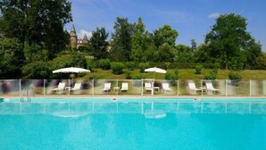 A swimming pool with lounge chairs and umbrellas, surrounded by a fence, with a castle in the background. - Chateau de Castel Novel (Saint-Pantaleon-de-Larche)