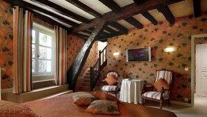 A cozy room with a bed, two chairs, a small table, a TV, and a staircase. - Chateau de Castel Novel (Saint-Pantaleon-de-Larche)