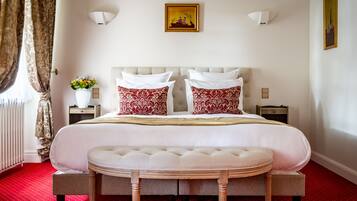Un lit bien fait, avec des oreillers blancs et rouges, une table de chevet ornée d’un vase de fleurs et une lampe fixée au mur.