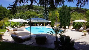 Un patio trasero con piscina, rodeado de sillas de descanso y sombrillas.