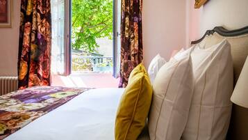 Een hotelkamer met een bed, bloemen gordijnen en uitzicht op een balkon met groen.