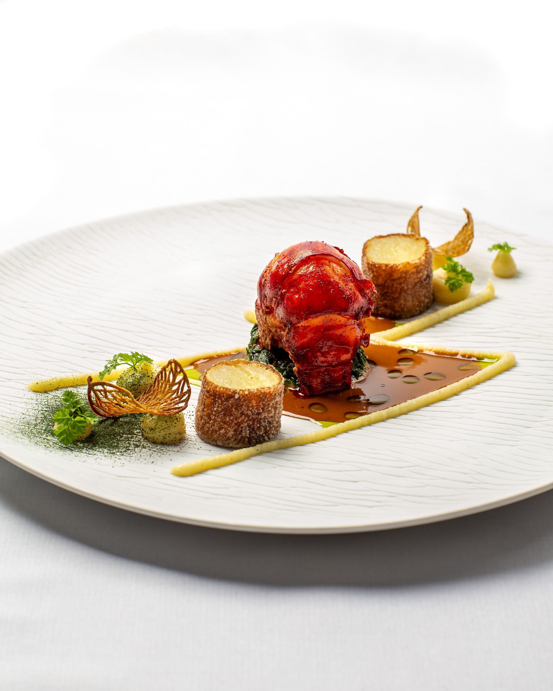 A white plate with a dish of food, including a red item, a cylindrical item, and some green garnish.