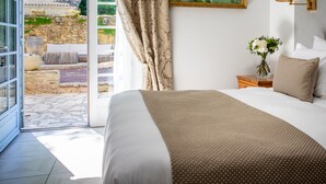 Un dormitorio con una cama grande, un cuadro en la pared, una mesita de noche con una lámpara y vistas a un jardín a través de una puerta abierta.