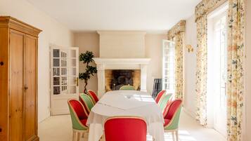 A dining room with a white table, red and green chairs, a wooden cabinet, and a fireplace.