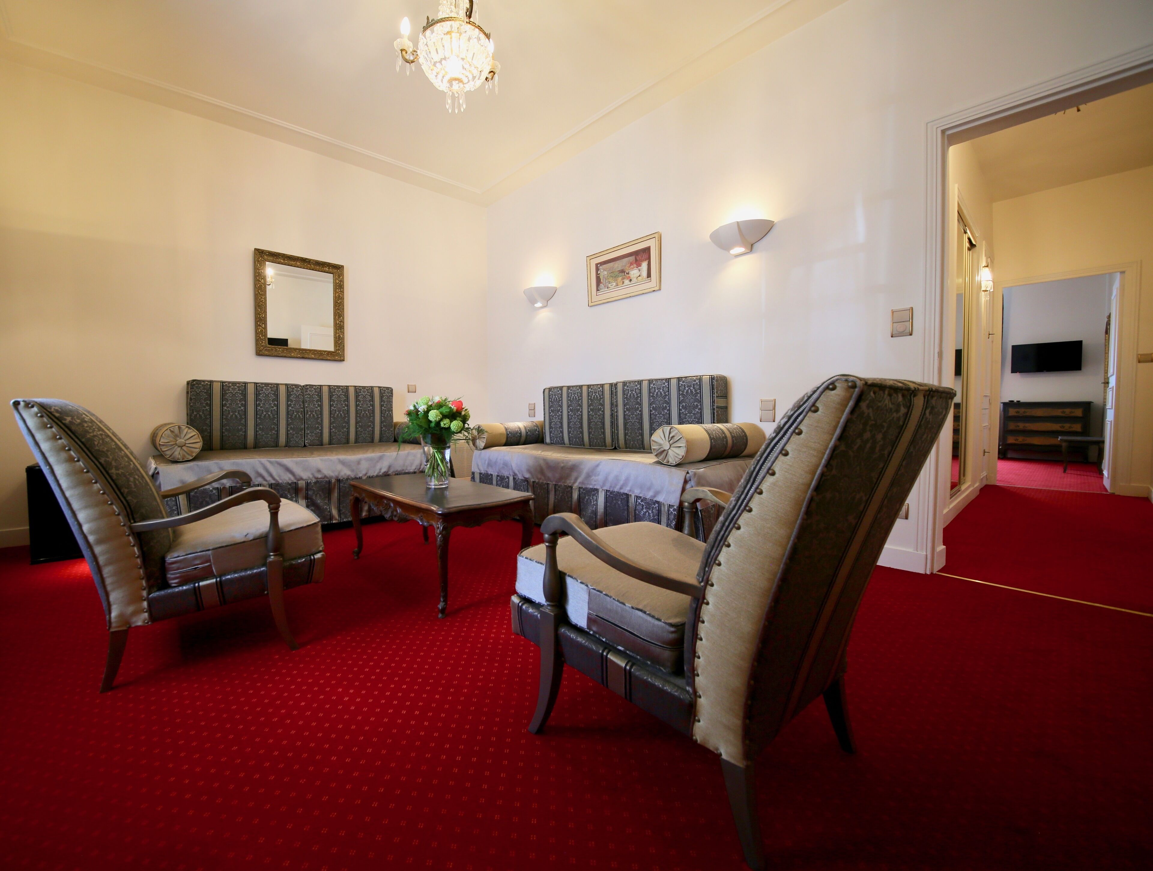 A room with a red carpet, two sofas, a table with a vase, and a chandelier.