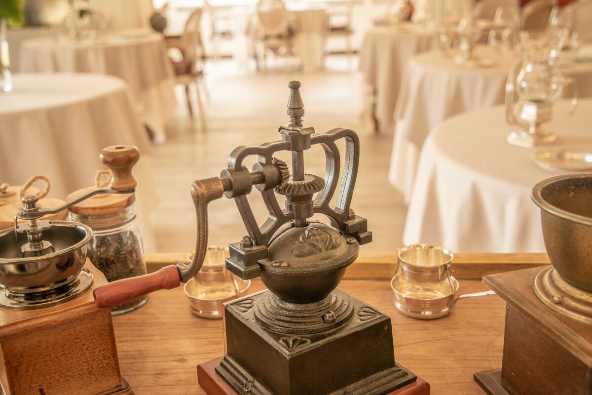 A vintage coffee grinder on a wooden table in a restaurant setting.