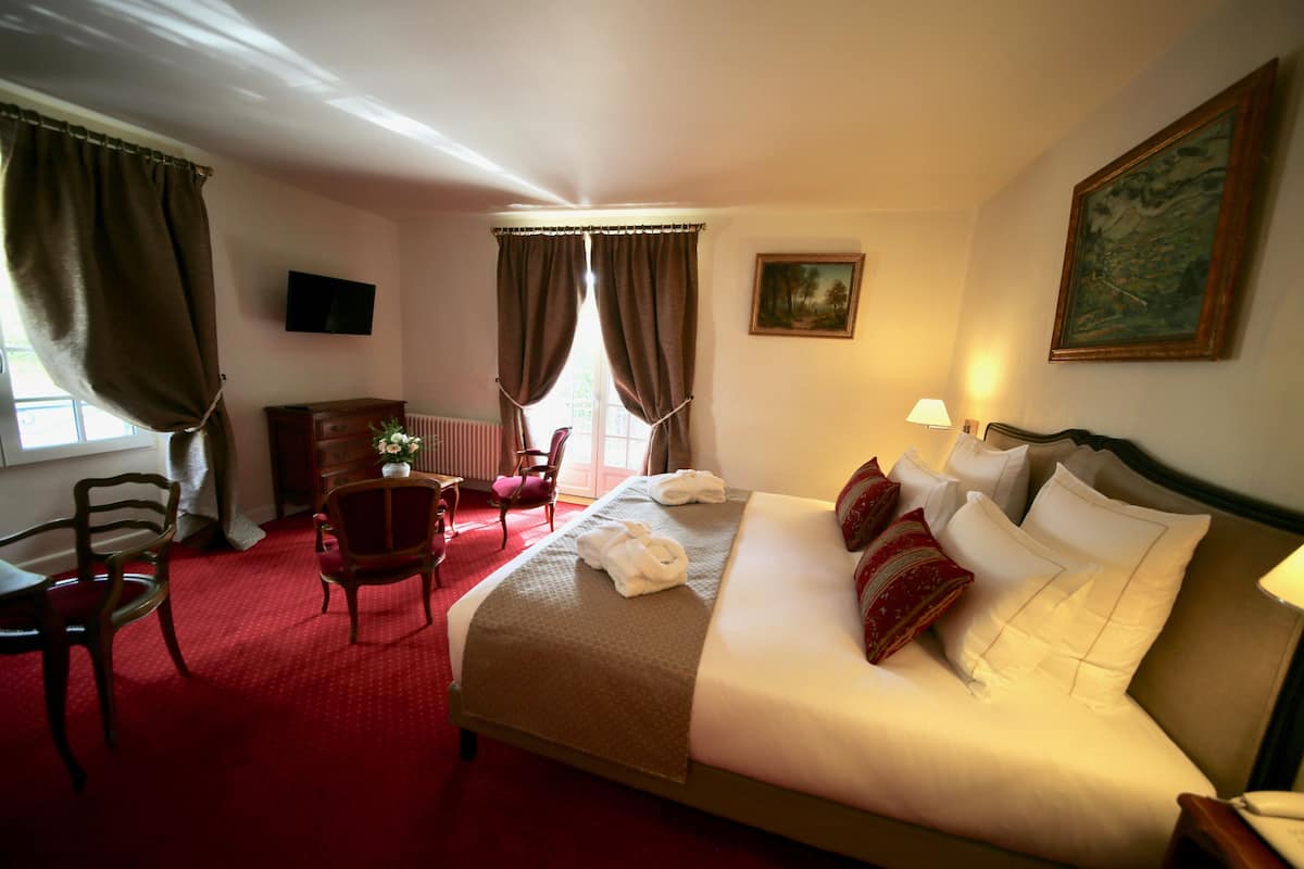 Habitación de hotel con cama, escritorio, silla, radiador, televisor y un cuadro en la pared.