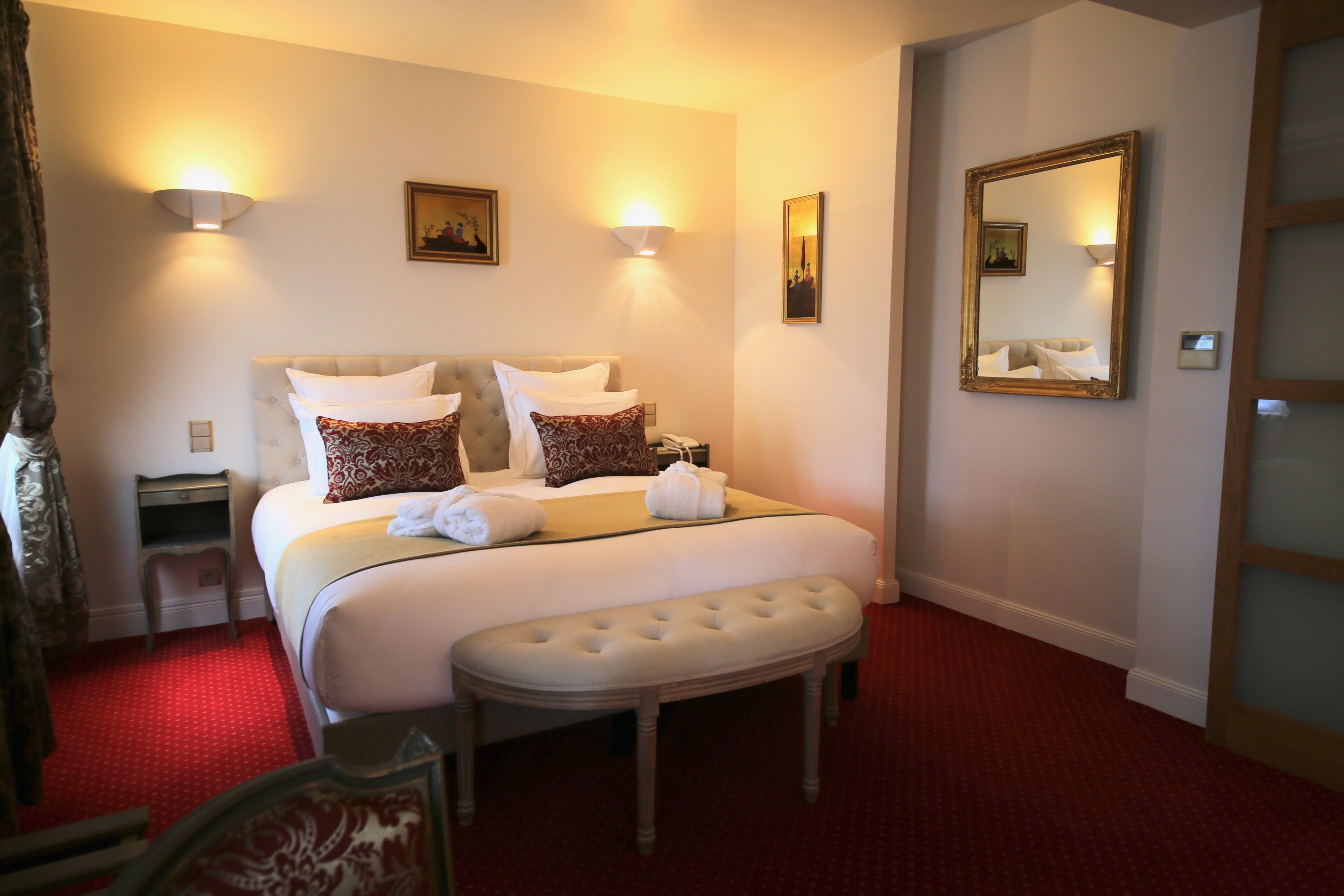 Une chambre d’hôtel avec un grand lit, deux lampes de chevet, une table de chevet, un banc et un miroir au mur.