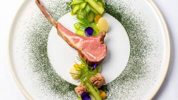 A plate with a lamb chop, asparagus, and potatoes, garnished with herbs and flowers.