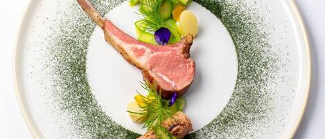 Une assiette contenant une côte d’agneau, des asperges et des pommes de terre, le tout agrémenté d’herbes et de fleurs.