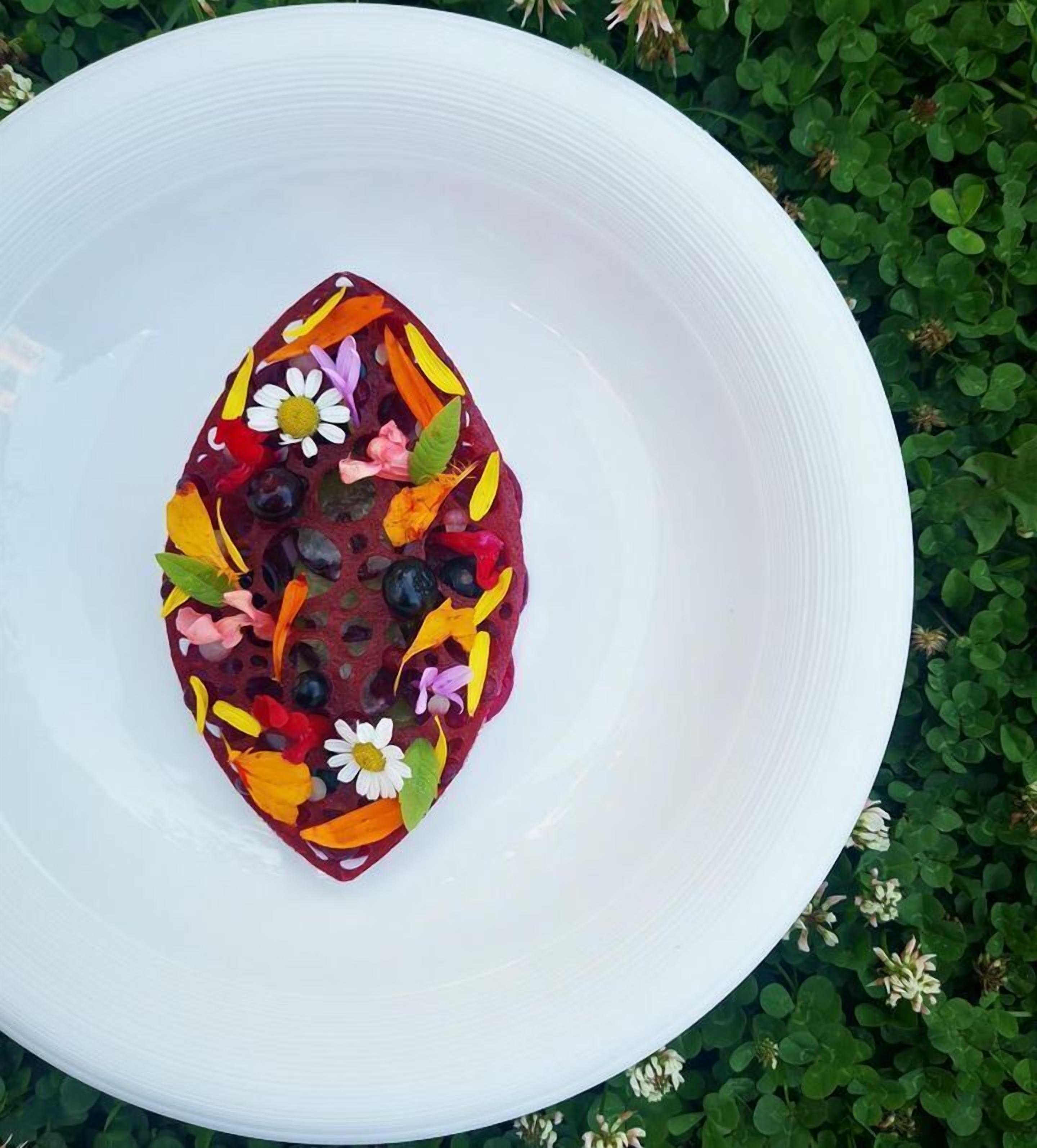 Un tazón blanco con una decoración colorida de frutas y flores sobre un fondo de hojas verdes.