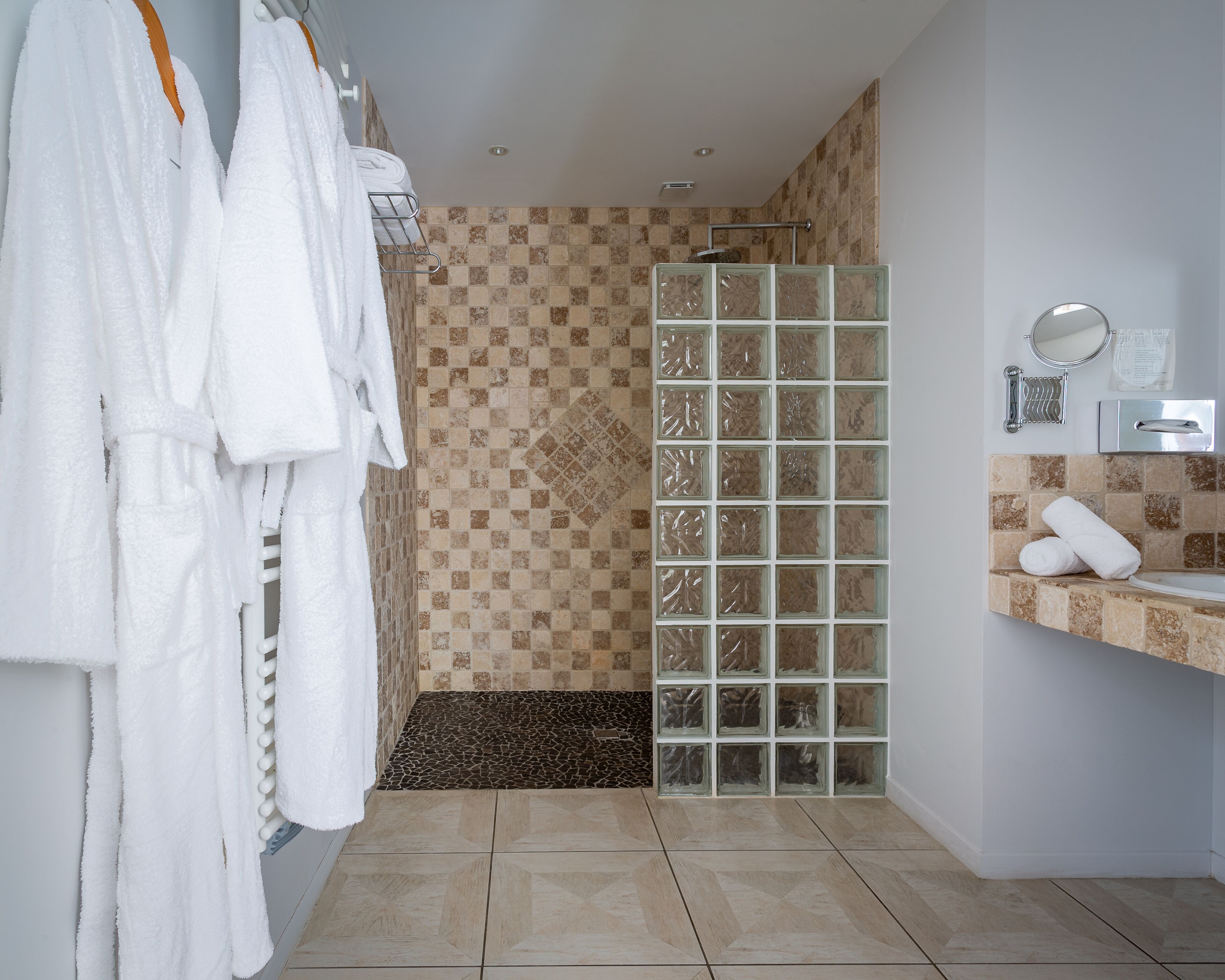 Un baño con ducha, paredes de azulejos, un lavabo con espejo y toallas en un escurridor.
