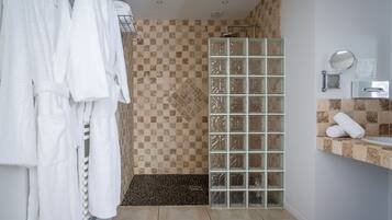 Un baño con ducha, paredes de azulejos, un lavabo con espejo y toallas en un escurridor.