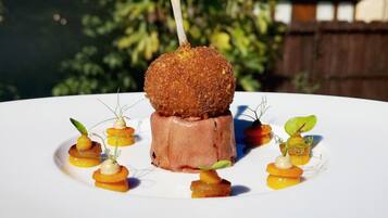 Un plato blanco con un guiso que incluye un alimento rebozado con un palillo, rodeado de pequeñas guarniciones sobre un plato blanco.