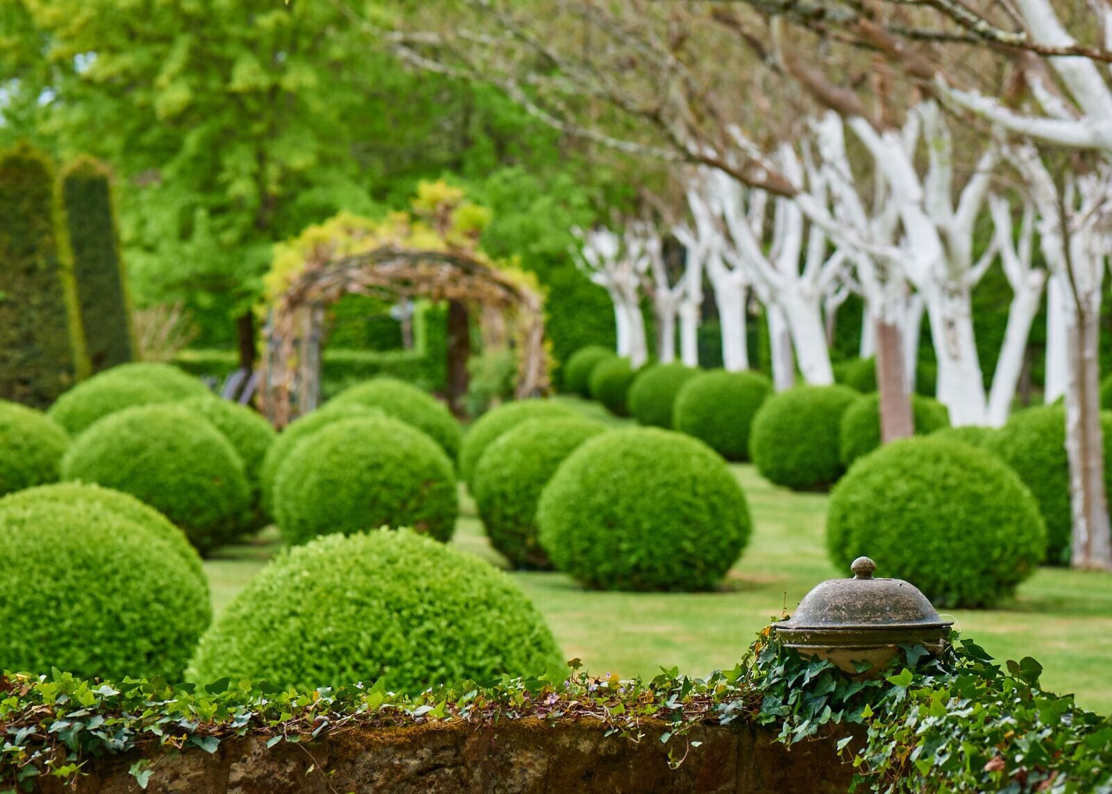 A well-manicured garden with neatly trimmed hedges and a stone structure.