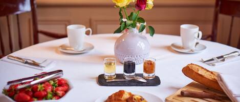A breakfast setting with a white tablecloth, a vase with yellow and red roses, a bowl of strawberries, a plate of pastries, and a loaf of bread.