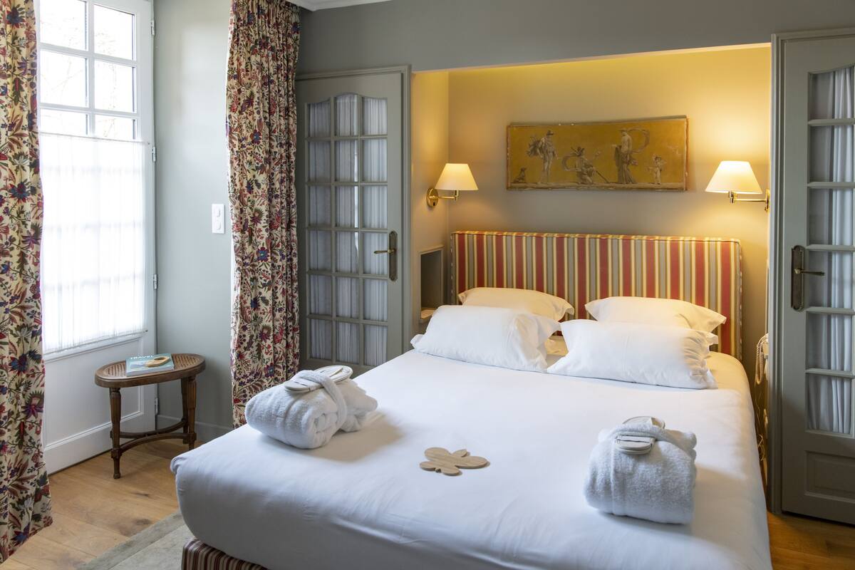 A hotel room with a large bed, two bedside lamps, a painting on the wall, and a door with a glass panel.