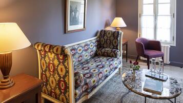 A room with a patterned sofa, a small round table with a book, a chair, and a lamp.