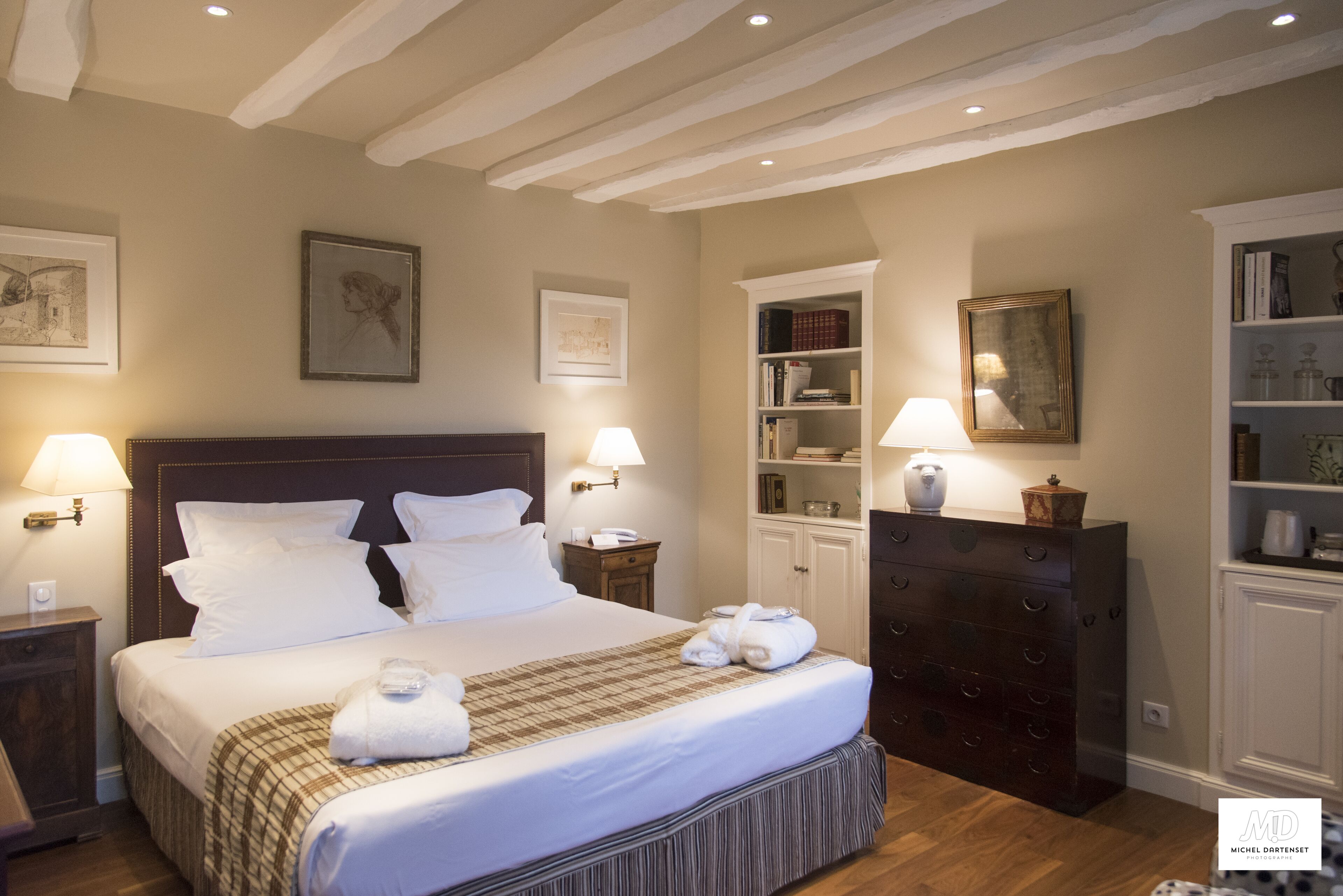 A neatly arranged hotel room with a large bed, bedside lamps, a dresser, and a bookshelf.