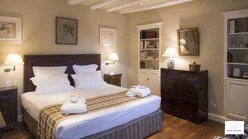A neatly arranged hotel room with a large bed, bedside lamps, a dresser, and a bookshelf.