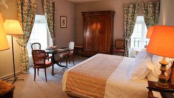 A hotel room with a bed, two chairs, a wooden wardrobe, and a table with a lamp.