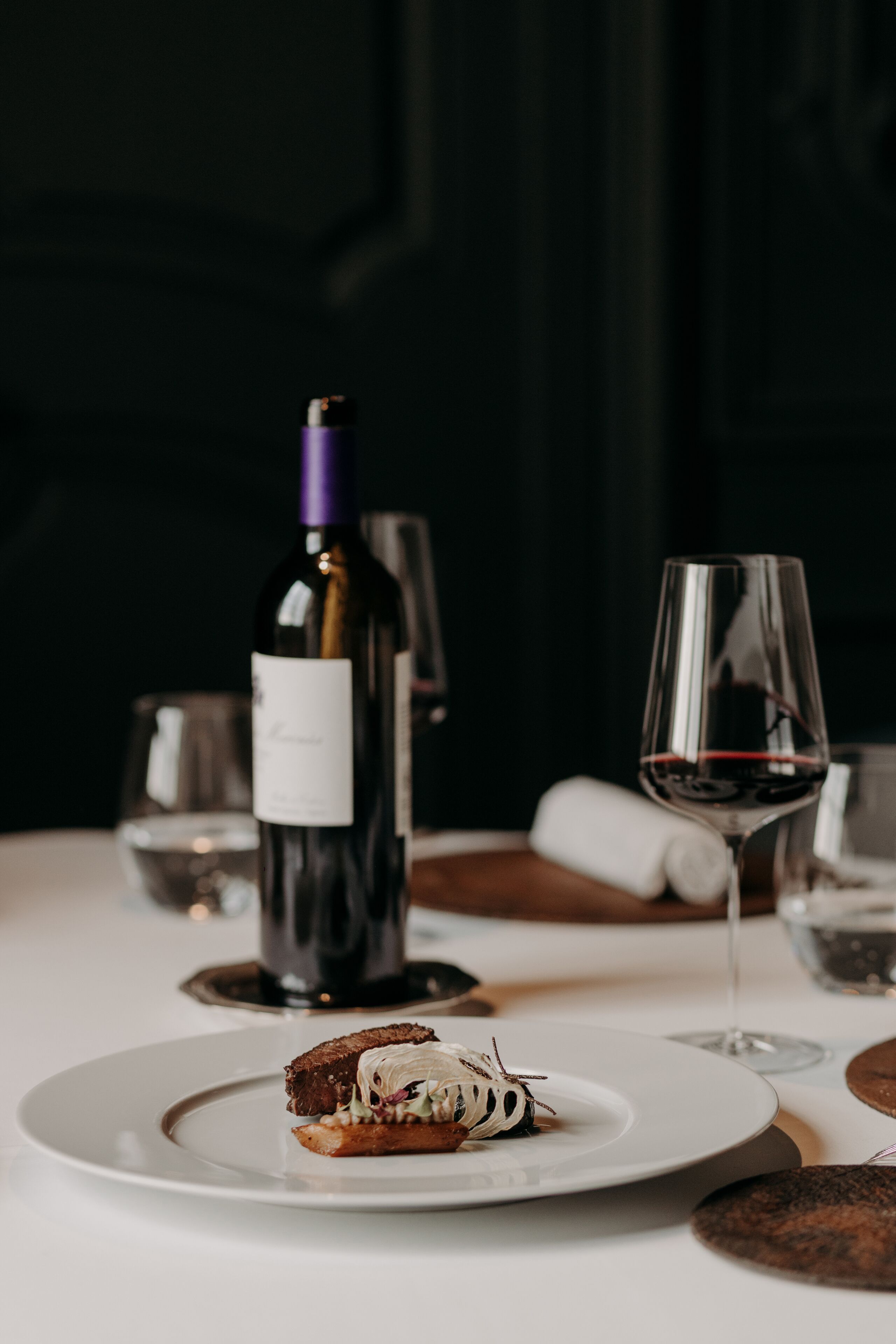 A dining table with a plate of food, a wine bottle, and a wine glass.