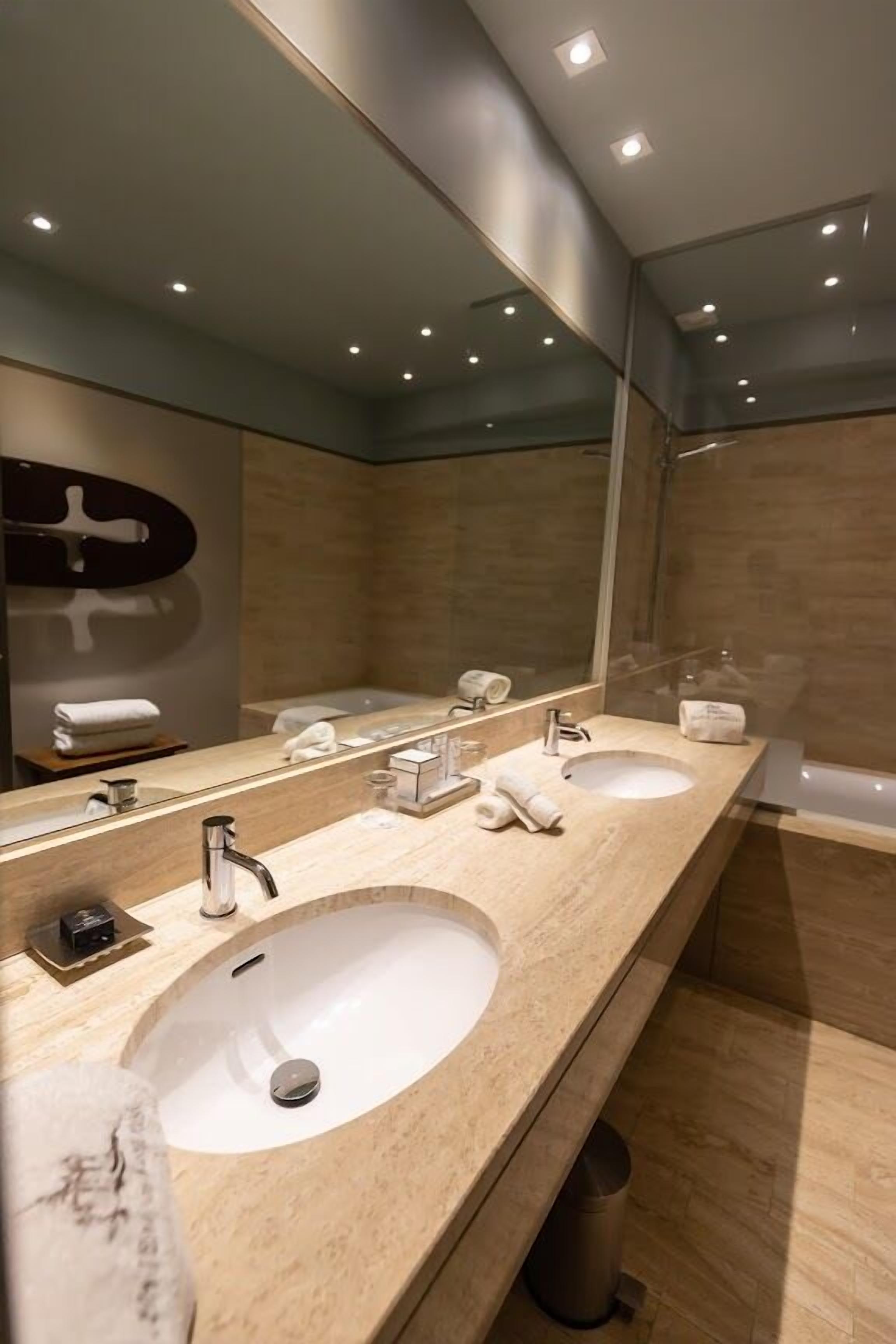 A modern bathroom with two sinks, a large mirror, and a bathtub.