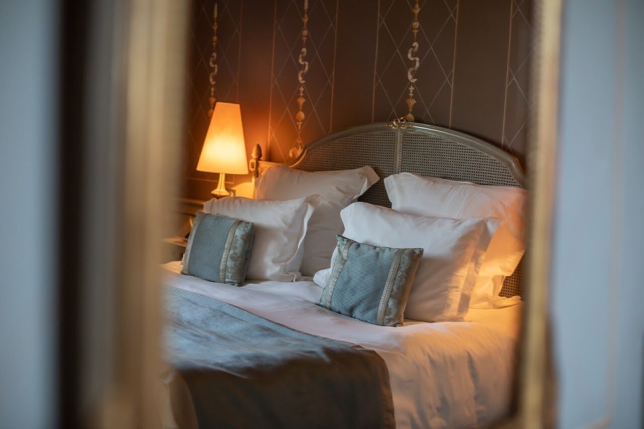 Una cama con almohadas blancas y azules, un colgante de luz y una mesita de noche con lámpara.