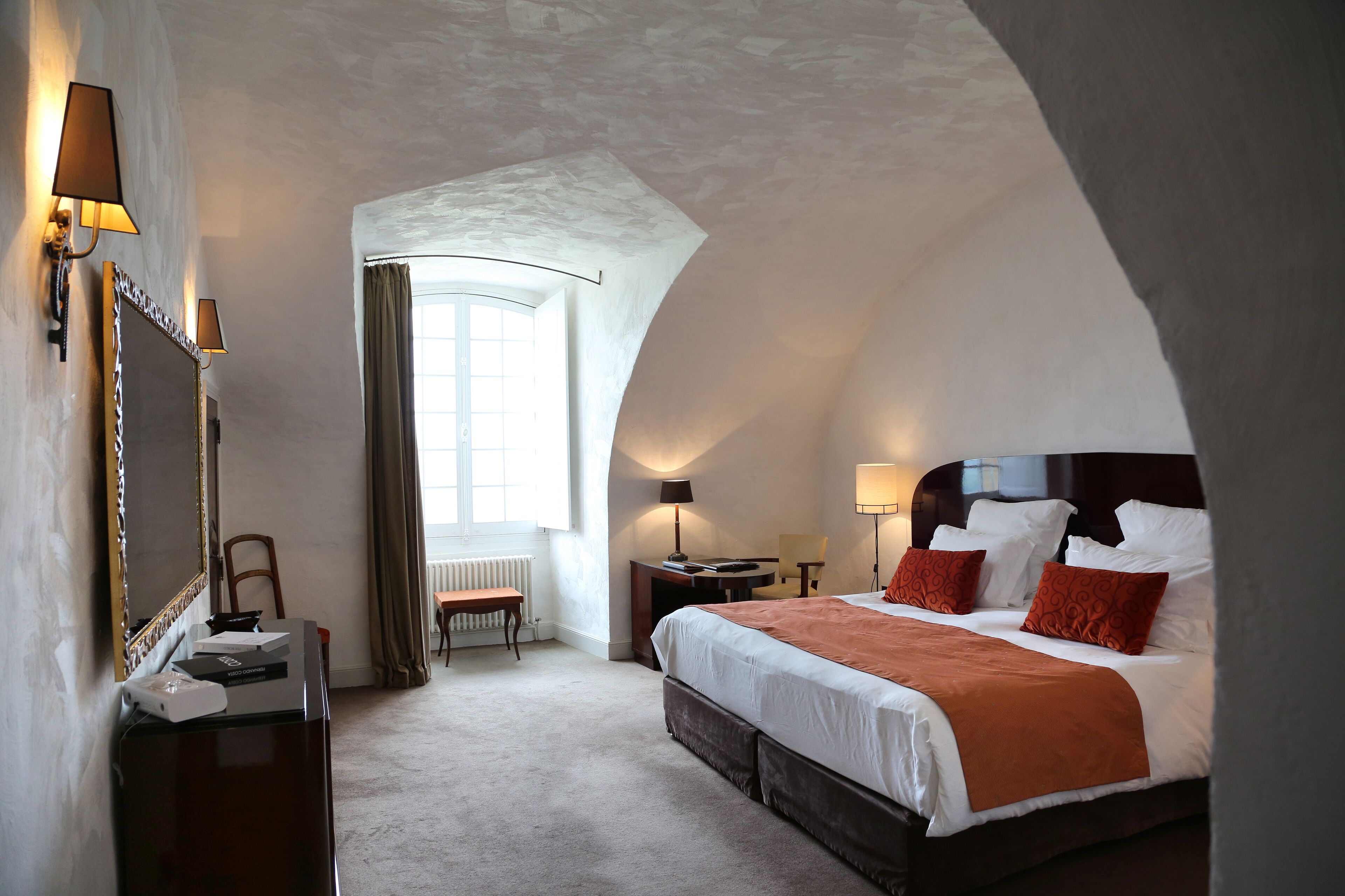 A hotel room with a large bed, a desk, a chair, and a mirror.