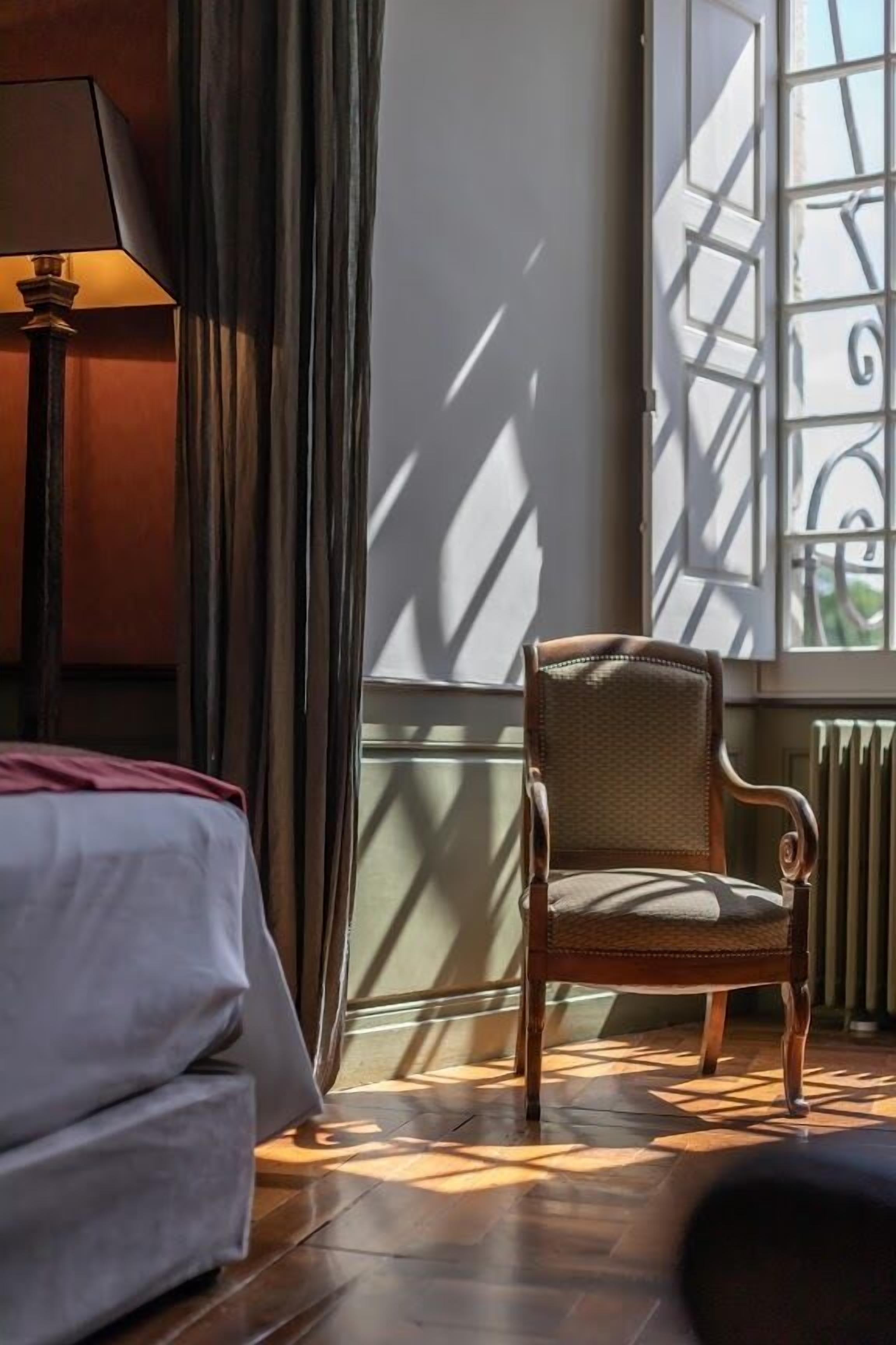 A hotel room with a bed, a chair, a window with a view of a building, and a radiator.