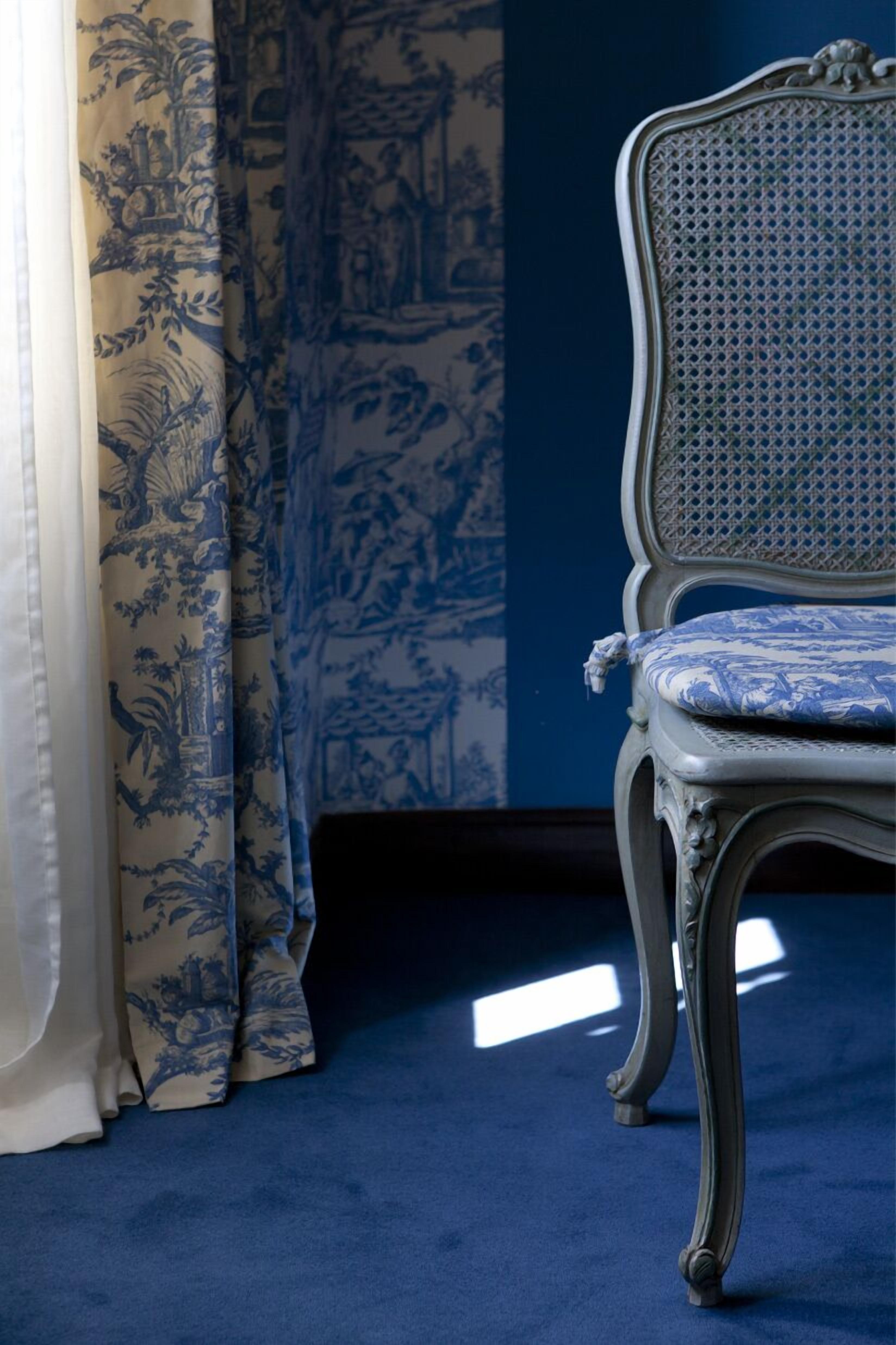 A chair with a patterned cushion, a blue wall, and patterned curtains.