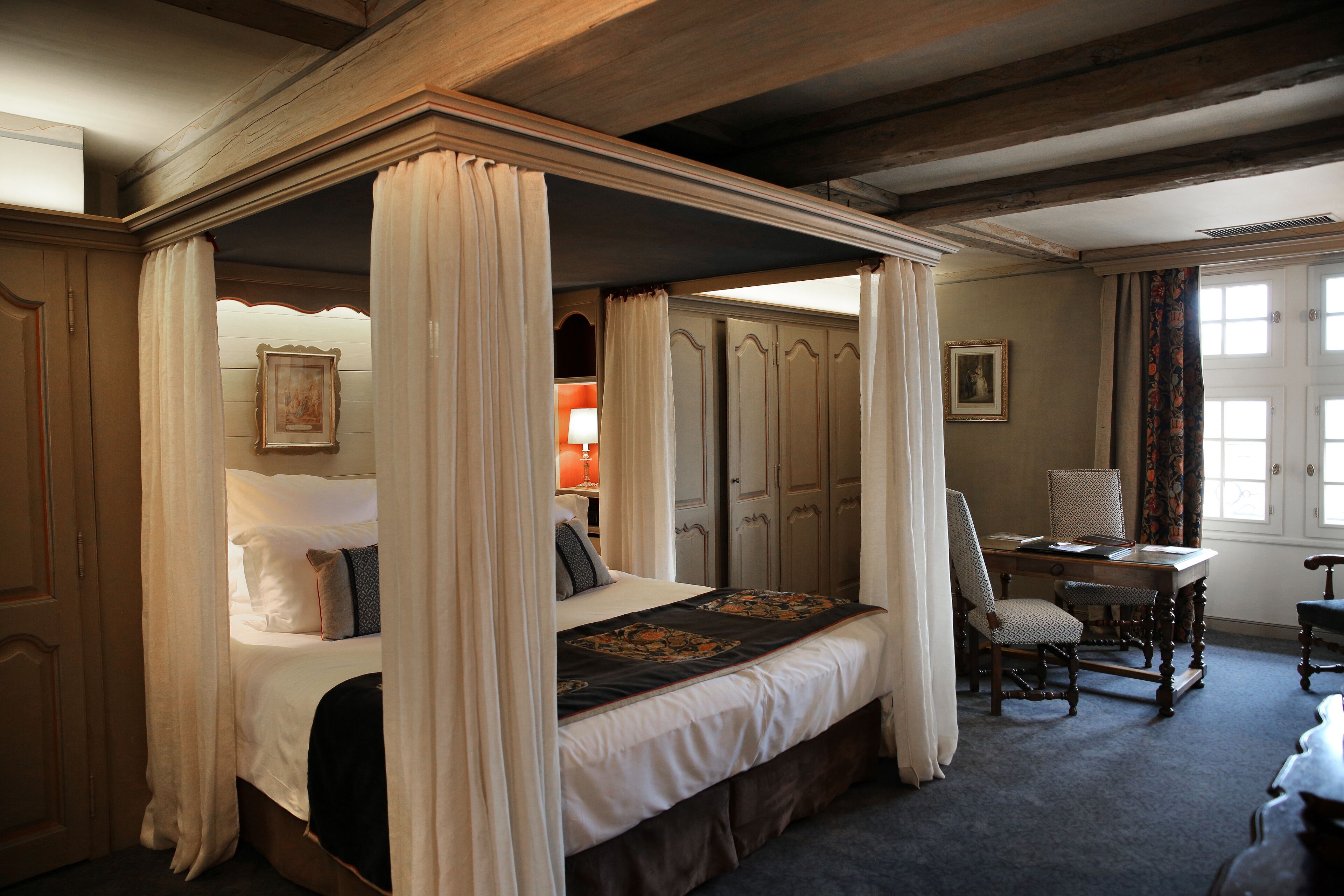 Un lit à baldaquin à quatre poteaux, avec un bureau et une chaise, une armoire et un tableau accroché au mur.