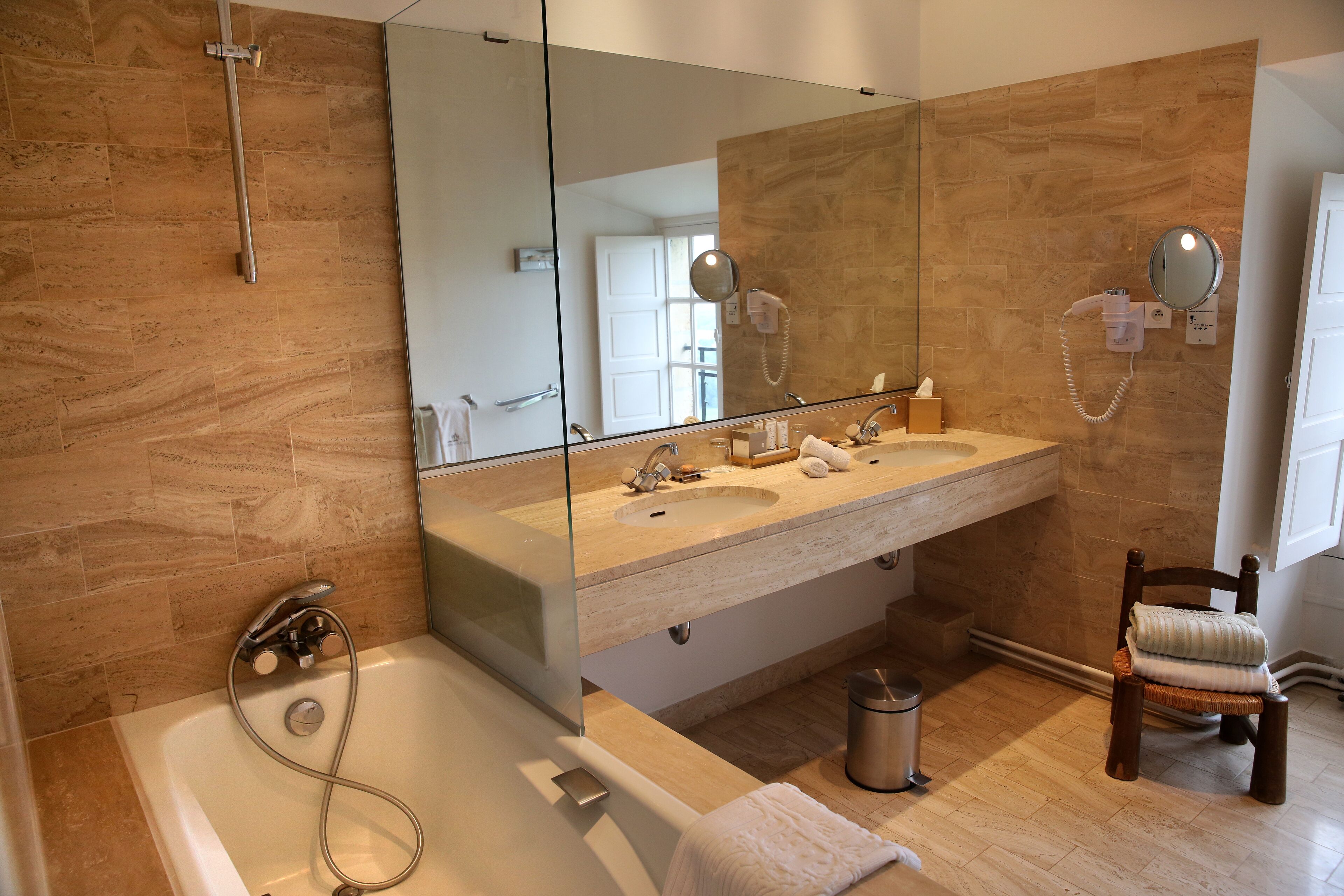 Une salle de bain moderne avec un grand miroir, deux vasques, une baignoire et un fauteuil.