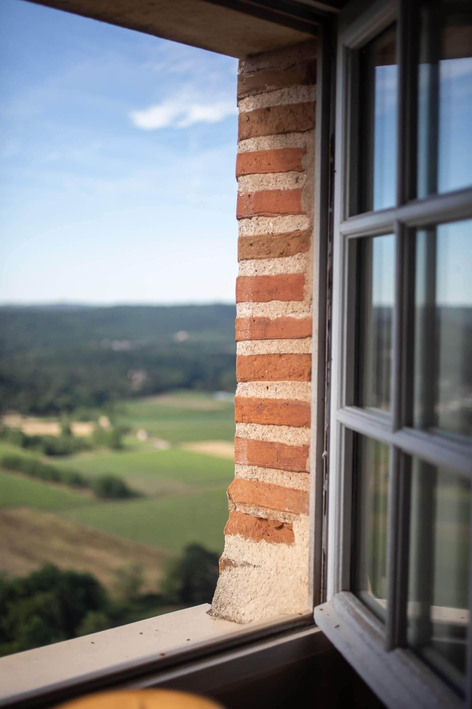 Una ventana que ofrece vistas a un muro de ladrillo y un paisaje.