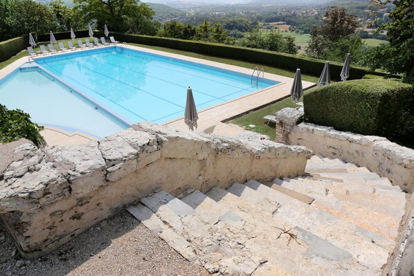 A swimming pool with steps leading down to it, surrounded by a stone wall and a view of the countryside.