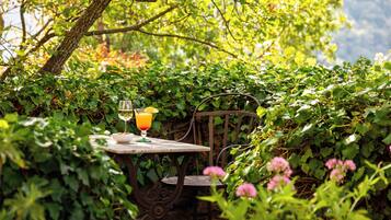 A table with a glass of orange juice and a glass of white wine, surrounded by greenery.